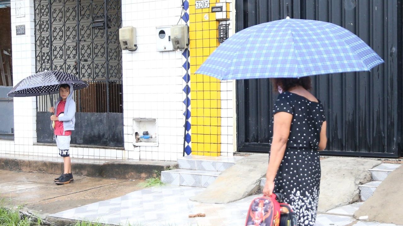 Idosa com guarda-chuva anda em direção a criança com guarda-chuva em Fortaleza