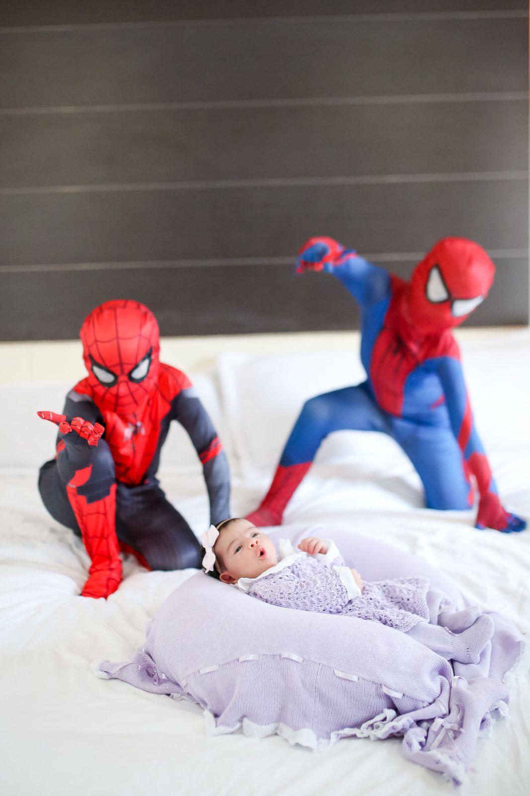irmãos vestidos de homem-aranha fazem poses do super-herói na cama, ao lado da irmã