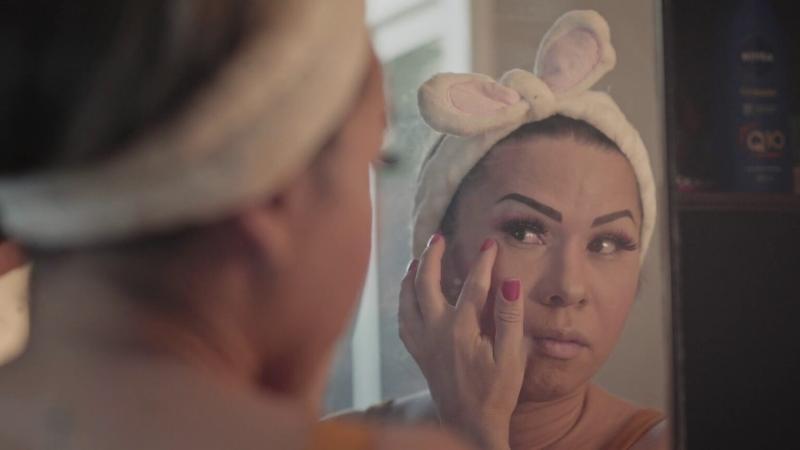 Mulher trans se maquiando em frente ao espelho