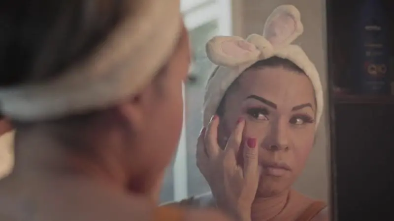 Mulher trans se maquiando em frente ao espelho