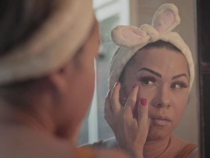 Mulher trans se maquiando em frente ao espelho