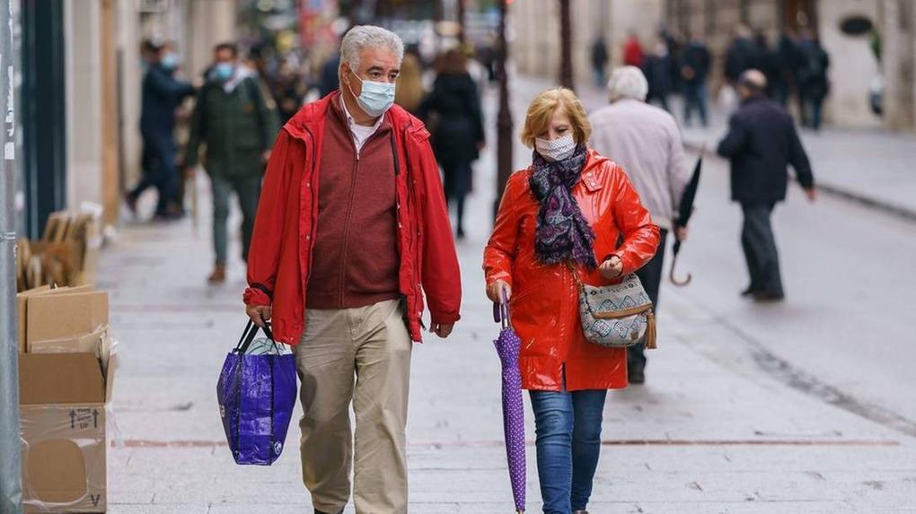 homem e mulher caminham de máscara em calçada