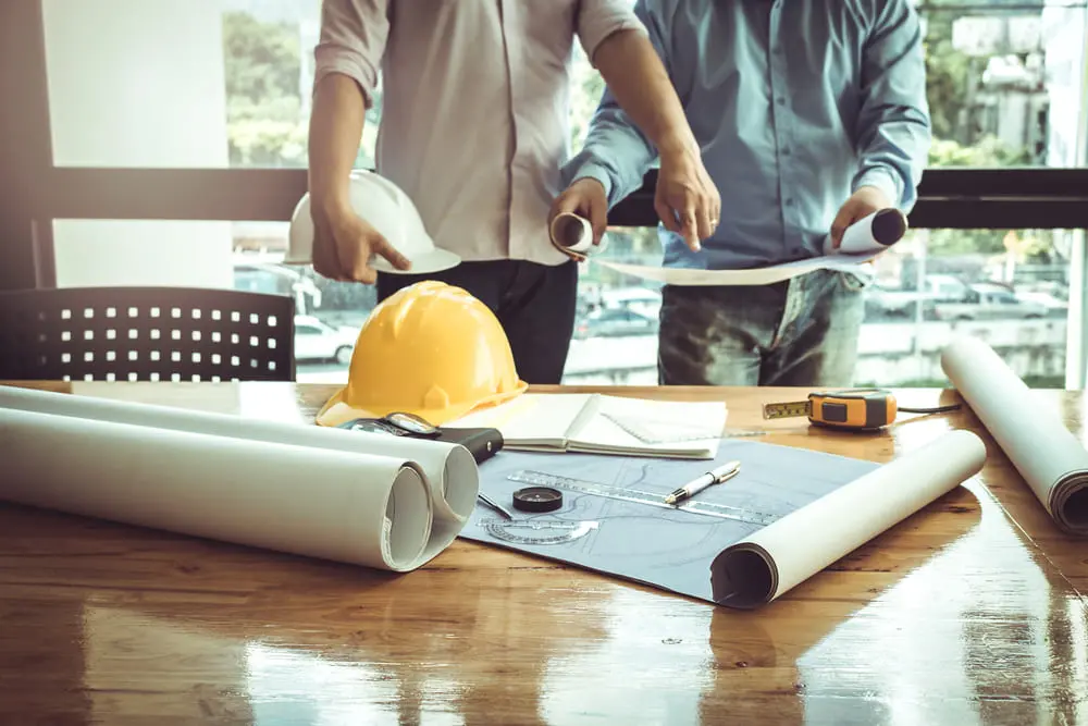 Homens apontando para folhas em mesa de projetos de arquitetura