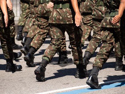 Grupo de militares com uniformes do Exército Brasileiro marchando de costas em rua