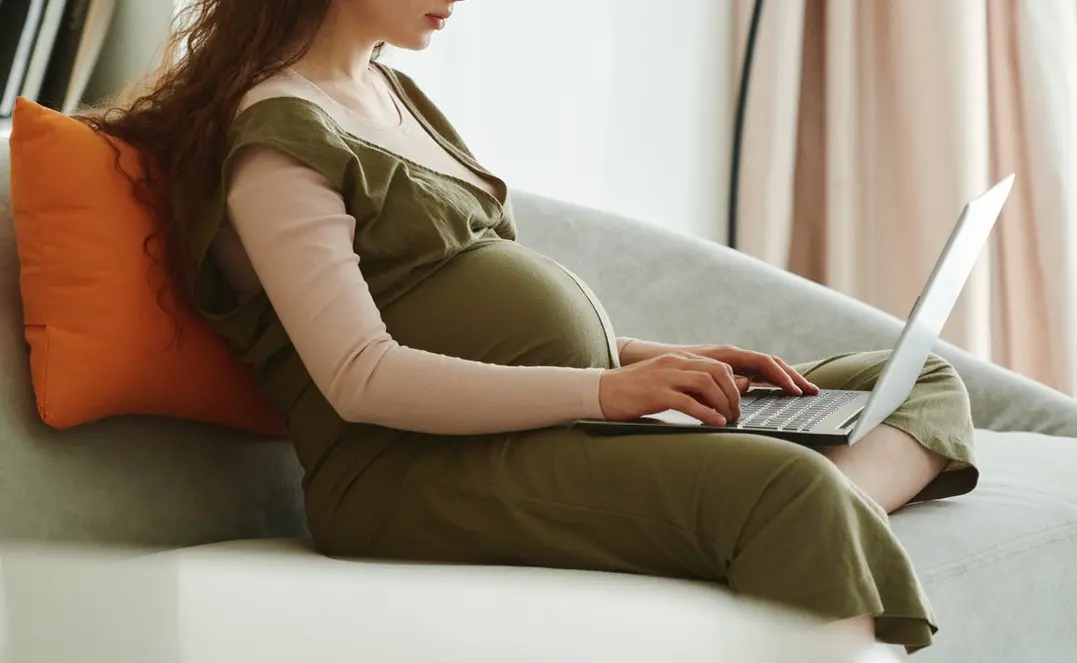 Mulher grávida sentada no sofá com notebook no colo