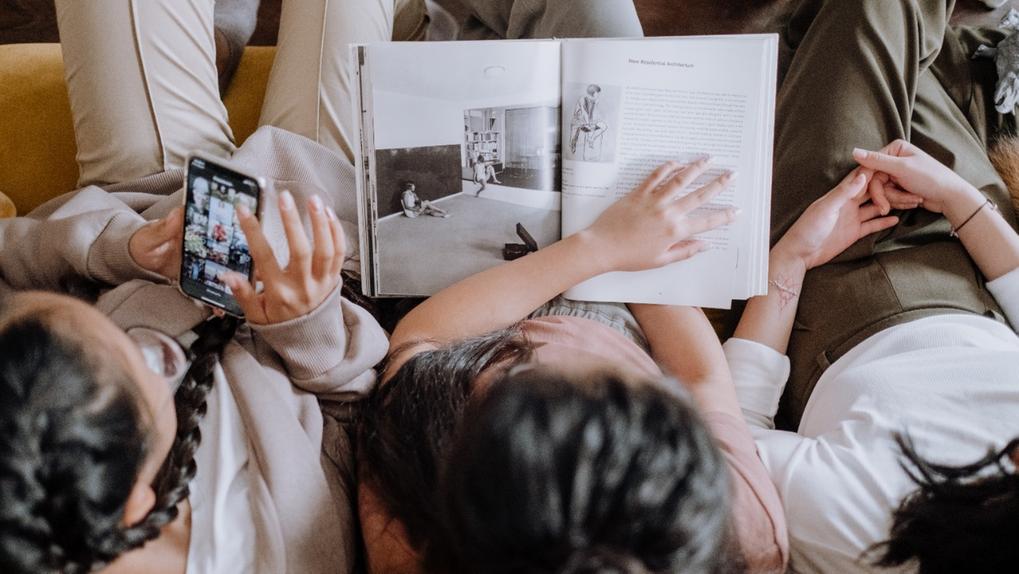 Mulheres sentadas num sofá com livros e celulares na mão
