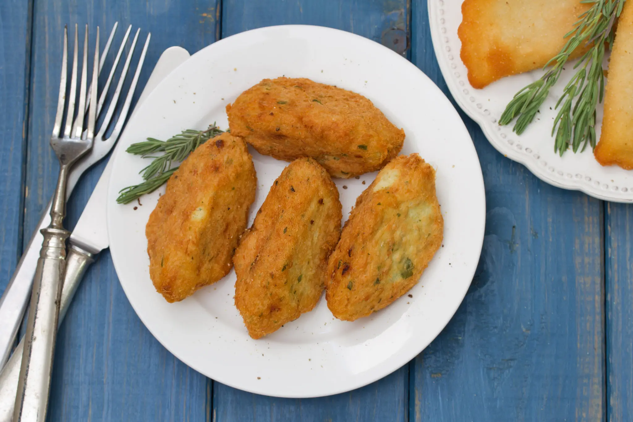 Croquete de peixe em um prato branco sobre um fundo amadeirado em tom de azul