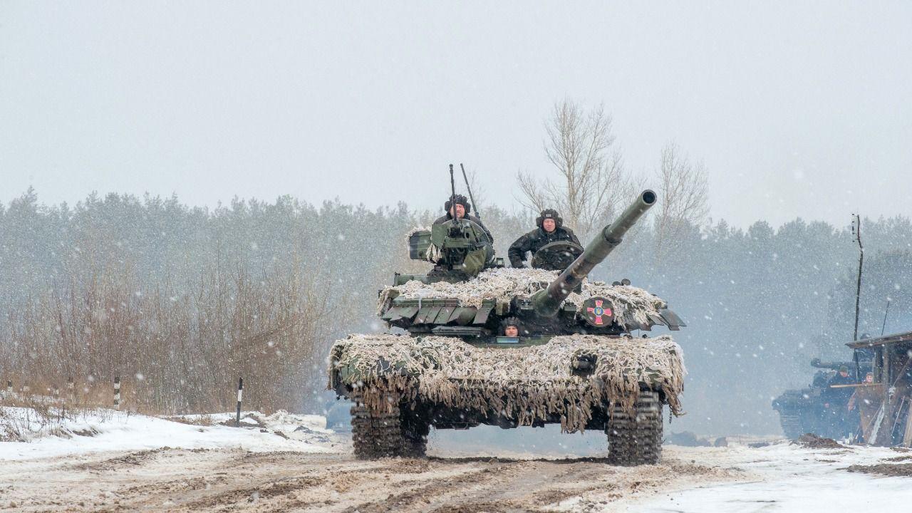 Militares estão em um tanque de guerra num cenário com neve caindo.