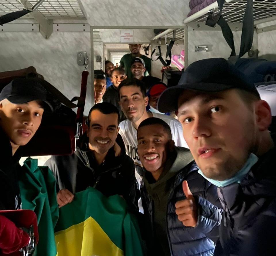 Jogadores brasileiros estão no trem, sorriem, enquanto deixam a Ucrânia