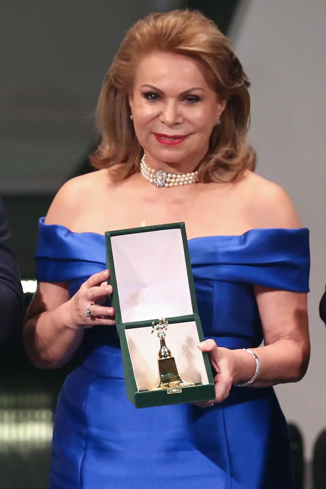 A desembargadora Iracema do Vale está de vestido azul. Ela está exibindo seu prêmio Sereia de Ouro.