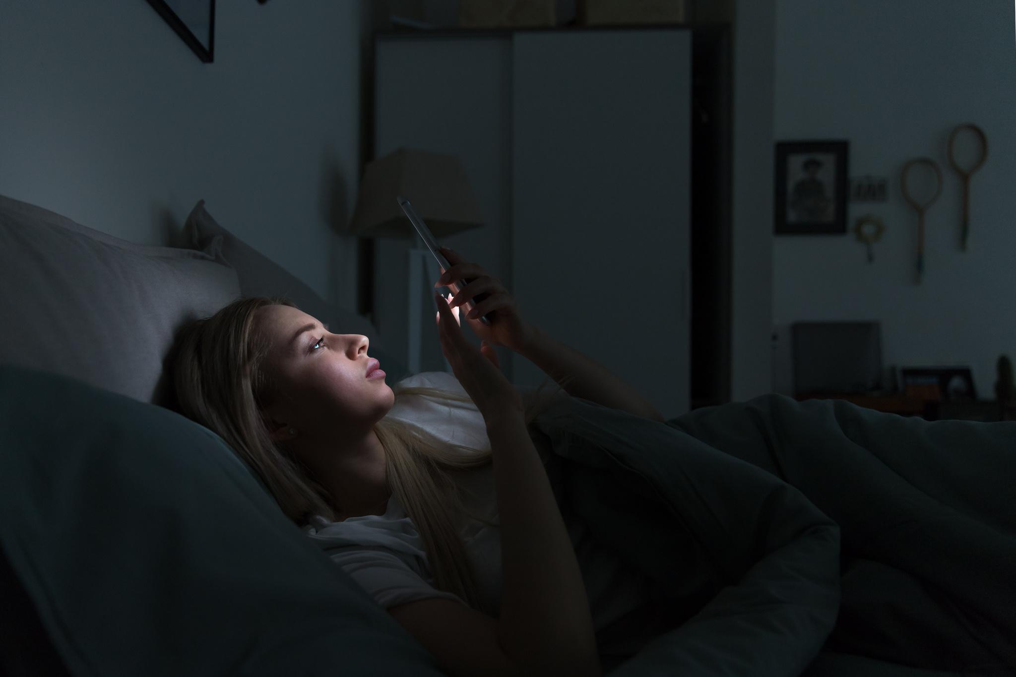 Mulher usa celular na cama antes de dormir