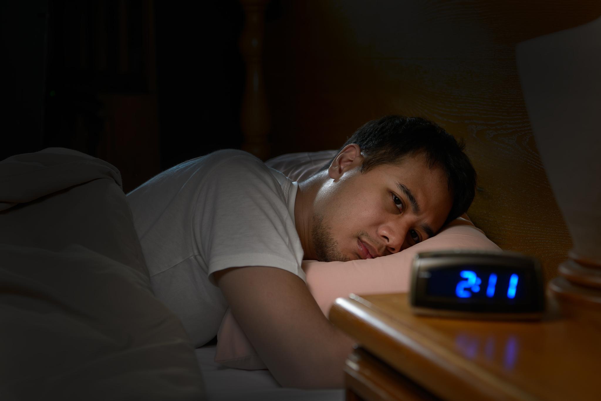 Homem com insônia deitando em uma cama olhando para um relógio