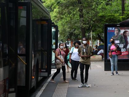 pessoas de máscara ao lado de ônibus em via de são paulo