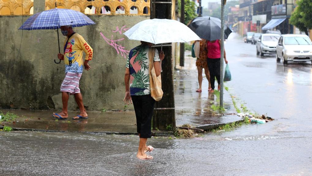 Pessoas com usando guarda-chuvas andam por rua alagada durante chuva em Fortaleza