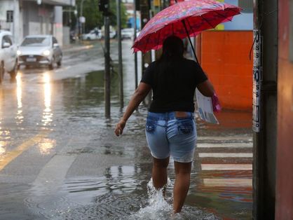Pessoa com guarda-chuva atravessa rua alagada em Fortaleza