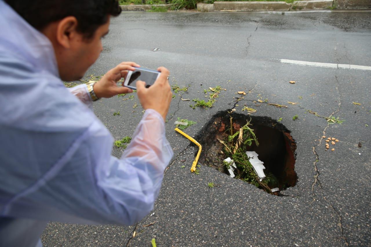 Imagem mostra pessoa fotografando cratera que abriu no viaduto da Oliveira Paiva, em Fortaleza, após forte chuna no dia 28 de março de 2022
