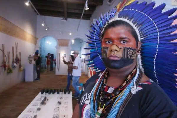 benício pitaguary de cocar e pintura indígena em destaque. ao fundo, uma exposição