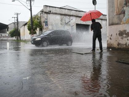 Pessoa usa guarda-chuva enquanto tenta atravessar rua alagada em fortaleza