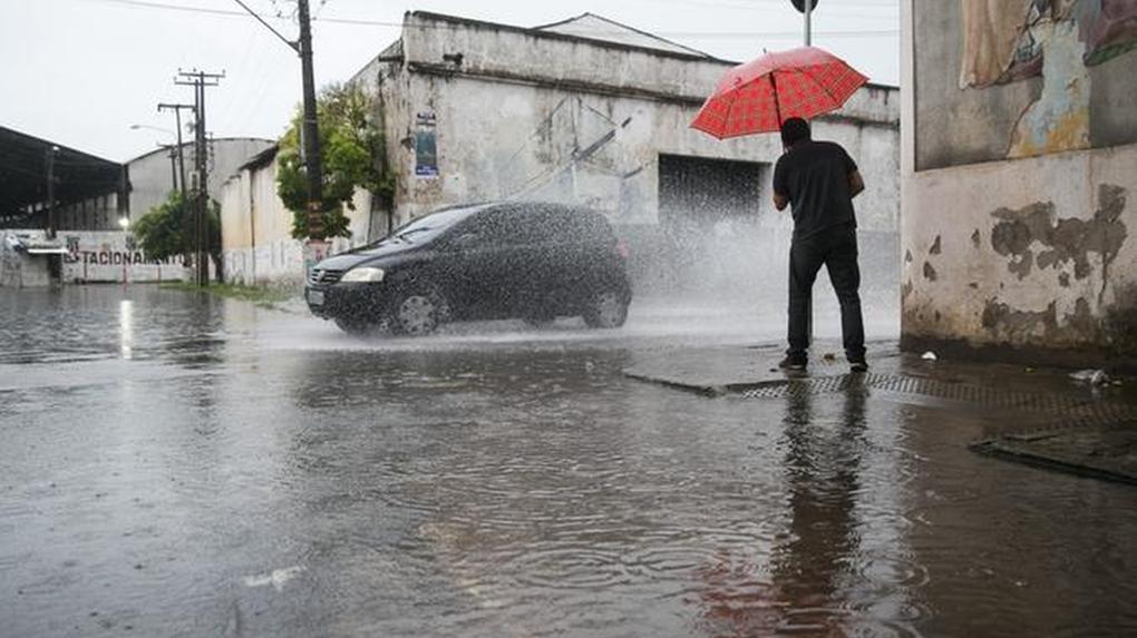 Pessoa usa guarda-chuva enquanto tenta atravessar rua alagada em fortaleza