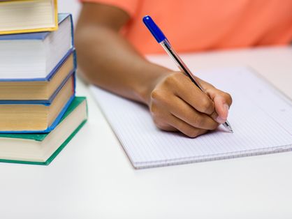 close-up da mão de uma jovem negra escrevendo para notebook com livros em casa