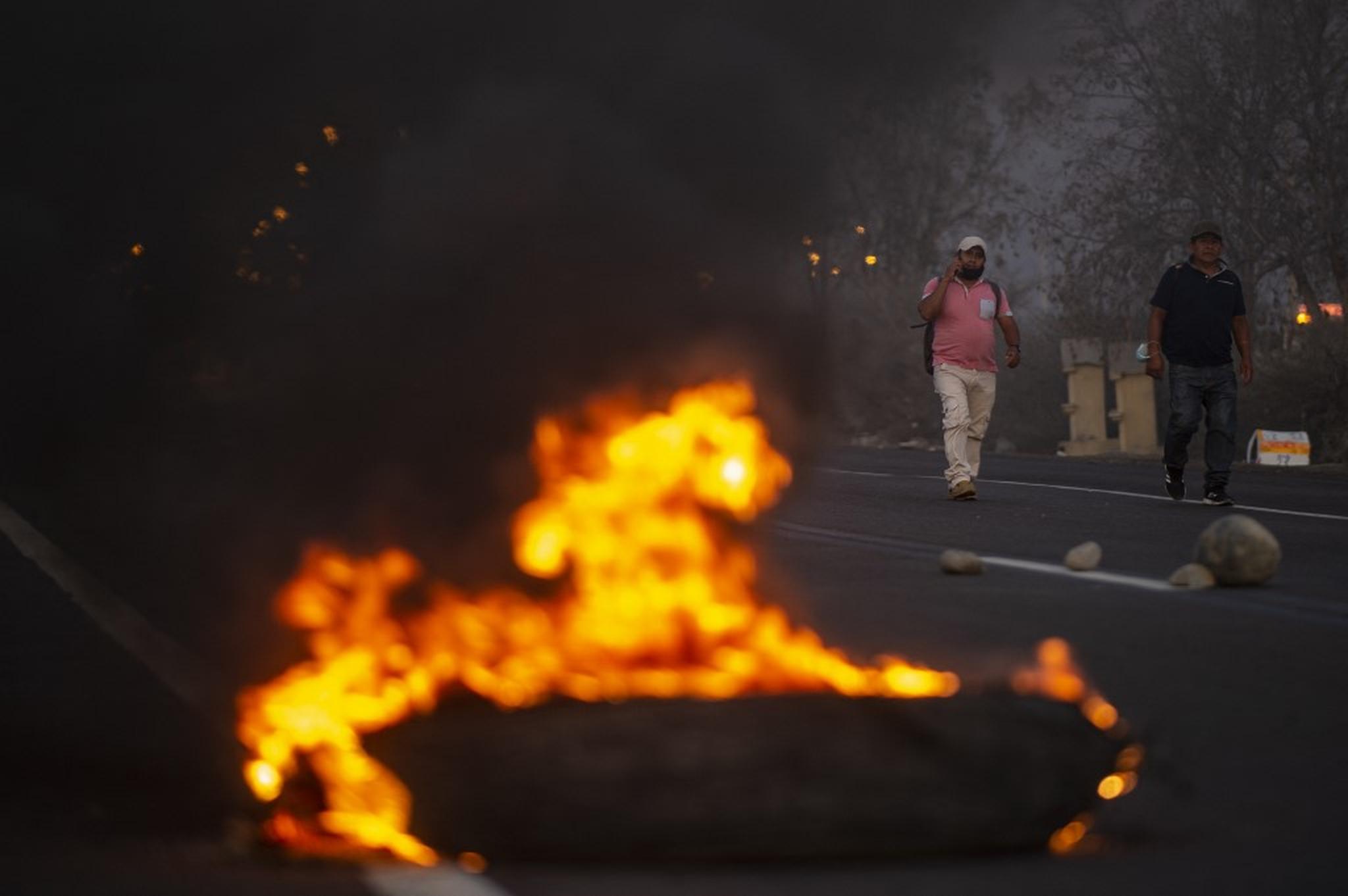 Homens caminham perto de pneus incendiados na rodovia Pan-Americana durante um bloqueio rodoviário no âmbito de uma greve parcial de transportadores de carga e passageiros, em Ica, no sul do Peru, em 4 de abril de 2022