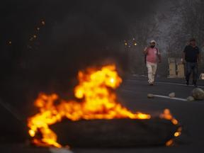 Homens caminham perto de pneus incendiados na rodovia Pan-Americana durante um bloqueio rodoviário no âmbito de uma greve parcial de transportadores de carga e passageiros, em Ica, no sul do Peru, em 4 de abril de 2022