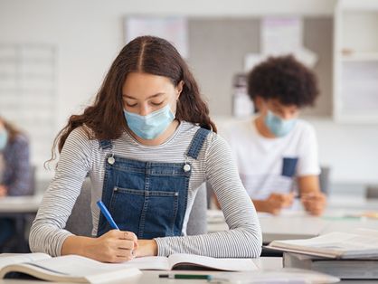 Estudante fazendo anotações enquanto usava máscara facial devido à emergência do coronavírus
