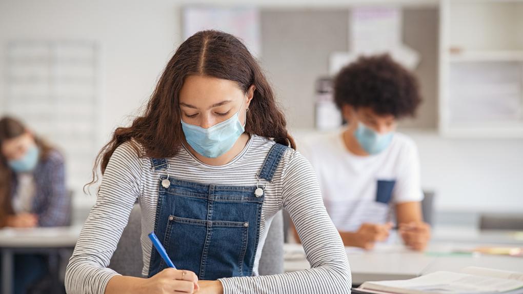 Estudante fazendo anotações enquanto usava máscara facial devido à emergência do coronavírus