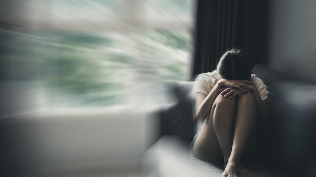 Conceito de ansiedade da mulher em posição fetal no sofá com cores sombrias.
