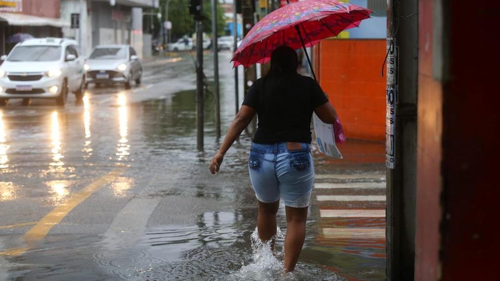 Pessoa com guarda-chuva atravessa rua alagada em Fortaleza