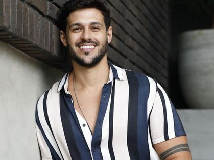 O ex-BBB Rodrigo Mussi está vestido com uma camisa de botão listrada azul e branco.