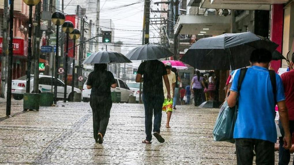 Pedestres transitam pelo Centro de Fortaleza em meio a chuva e usando guarda-chuvas