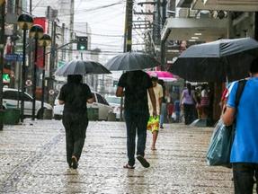 Pedestres transitam pelo Centro de Fortaleza em meio a chuva e usando guarda-chuvas