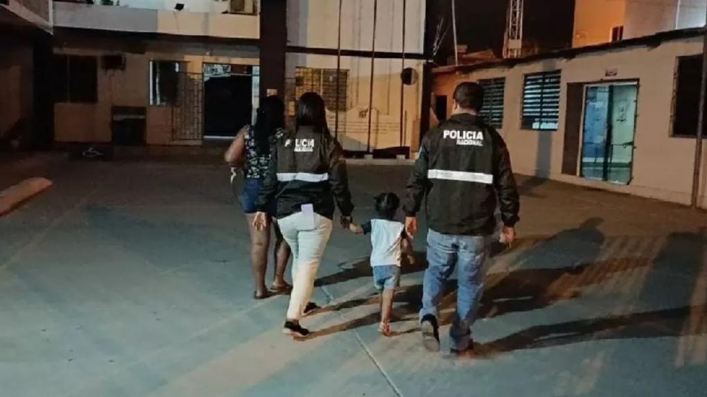 Menina que seria vendida no Equador ao lado de policiais e de uma mulher, todos de costas