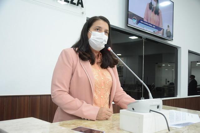 A vereadora Cláudia Gomes discursa na tribuna da Câmara Municipal de Fortaleza. Ela está vestida com uma camisa rosa e um sobretudo da mesma cor.