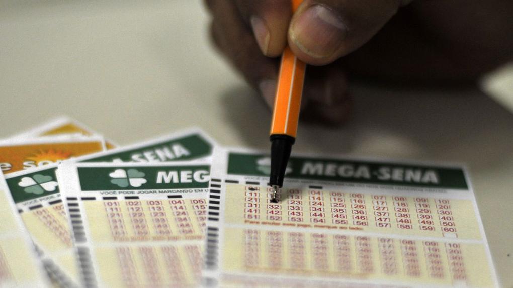 Close-up em mão usando caneta de cor preta para assinalar números em cartela de jogo da Mega-Sena