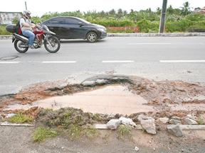 Motocicleta e carro trafegam ao lado de buraco com água da chuva acumulada