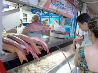 Vendedor de pescado no Mercado dos Peixes apresenta peixe para consumidores.