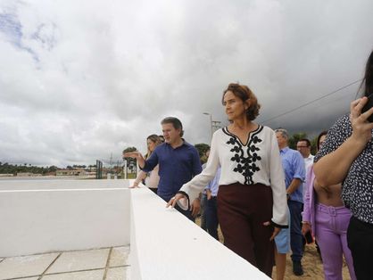 A governadora Izolda Cela aparece em primeiro plano, vestindo uma camisa branca e uma calça marrom, observando um sistema de abastecimento de água em Tianguá. O céu está nublado.