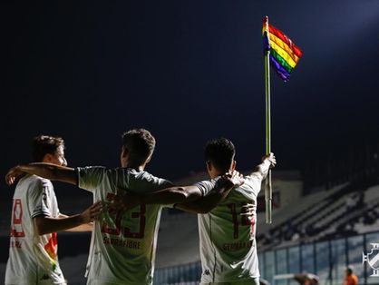 Imagem mostra jogadores abraçados e levantando a bandeira do arco-íris
