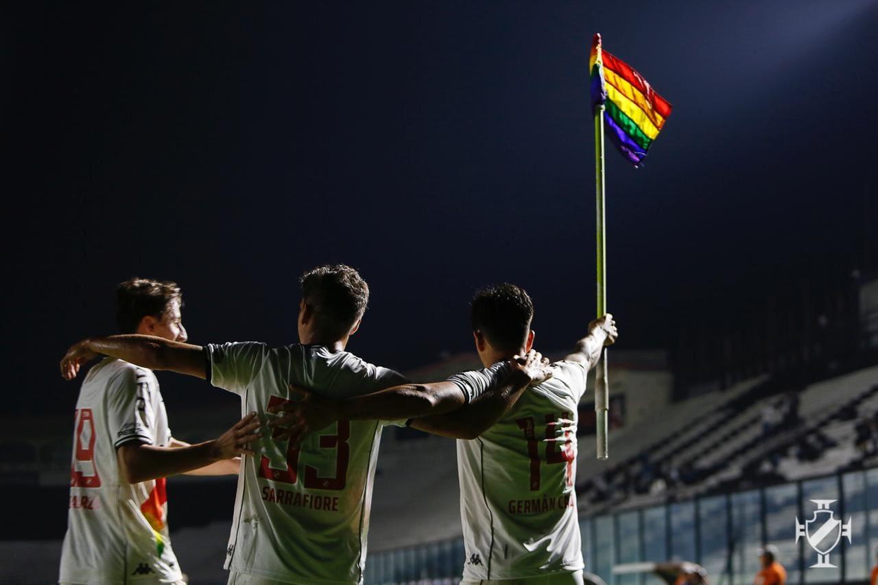 Imagem mostra jogadores abraçados e levantando a bandeira do arco-íris