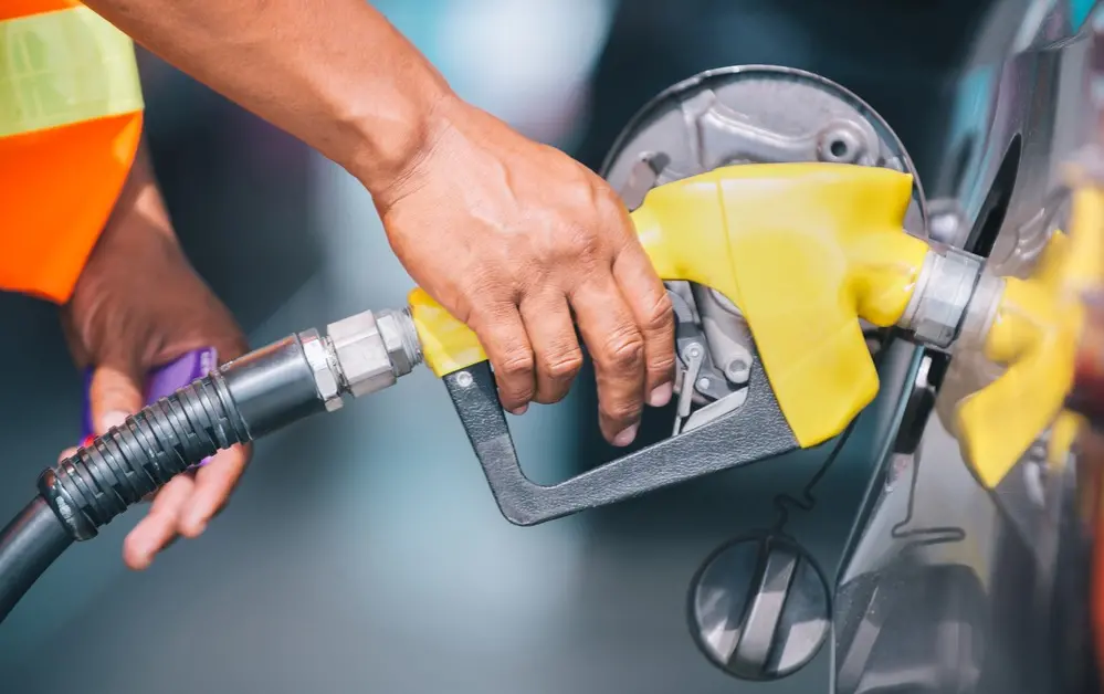 Mão segura uma bomba de gasolina da cor amarela.