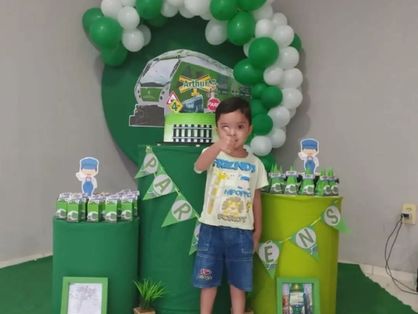 menino de quatro anos na frente de decoração do aniversário dele, que teve o tema metrofor, todo verde