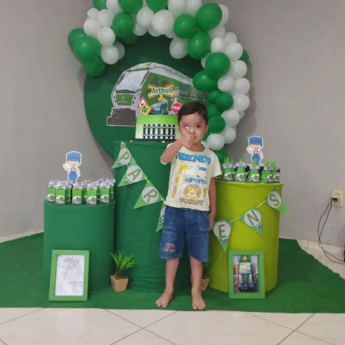menino de quatro anos na frente de decoração do aniversário dele, que teve o tema metrofor, todo verde