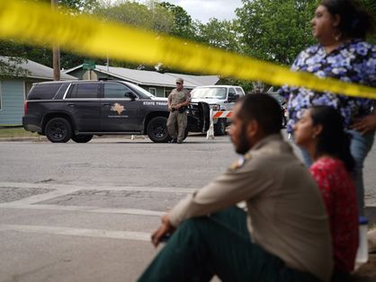 As pessoas sentam-se na calçada do lado de fora da Robb Elementary School enquanto soldados estaduais guardam a área em Uvalde, Texas, em 24 de maio de 2022