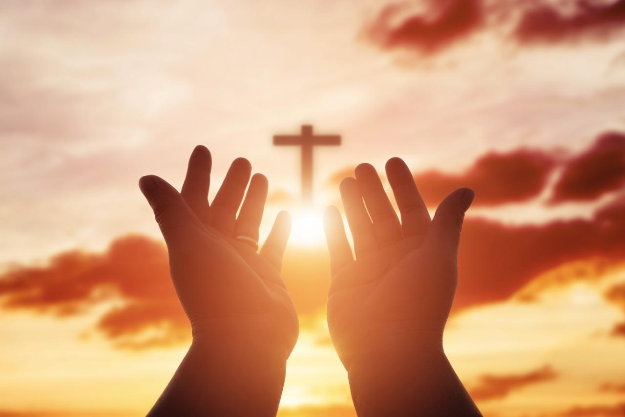 Cruz no céu e uma pessoa rezando com as mãos em direção ao símbolo religioso