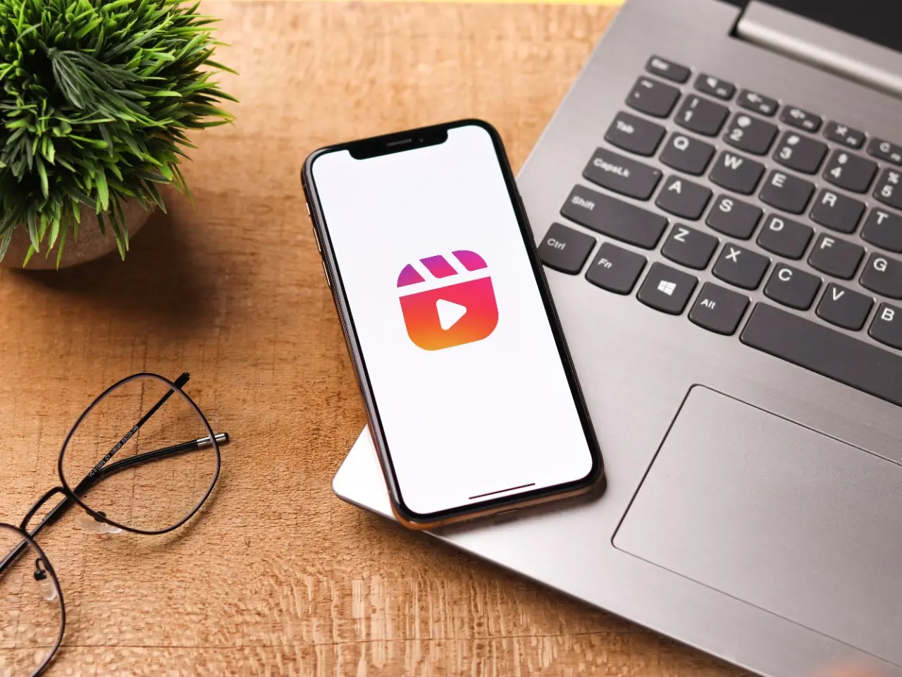 Celular com o aplicativo Instagram aberto ao lado de um computador, um óculos e uma plantinha