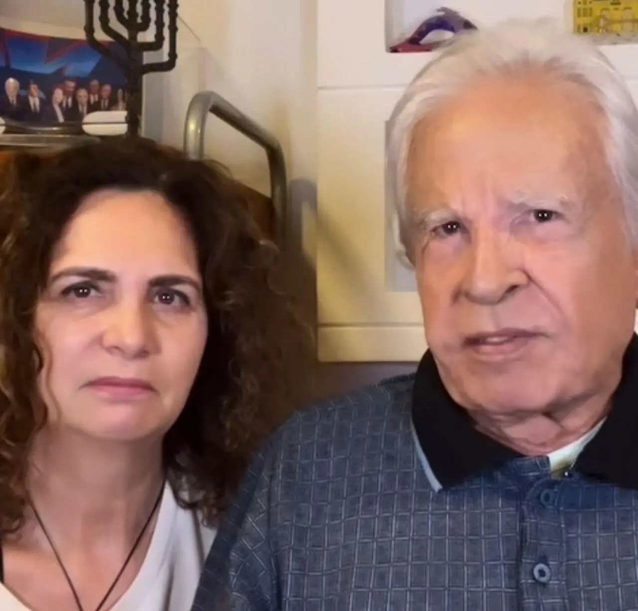 O casal Maria de Fátima, à esquerda, e Cid Moreira, à direita. Eles estão olhando para a câmera durante a gravação de uma live.
