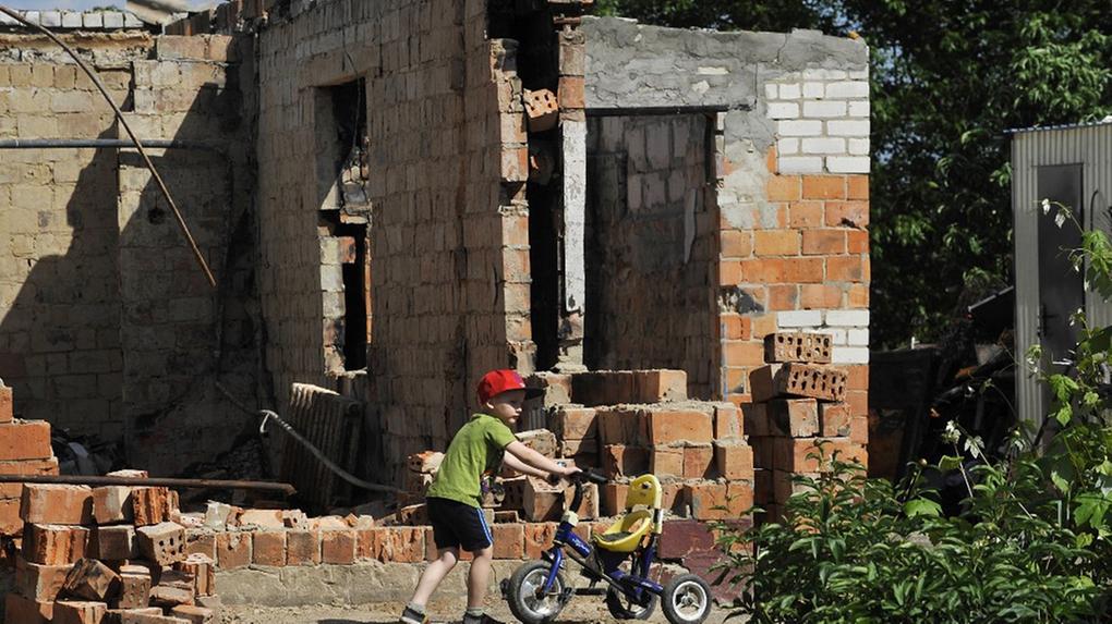 Menino empurra uma bicicleta em frente a um imóvel destruído na Ucrânia.