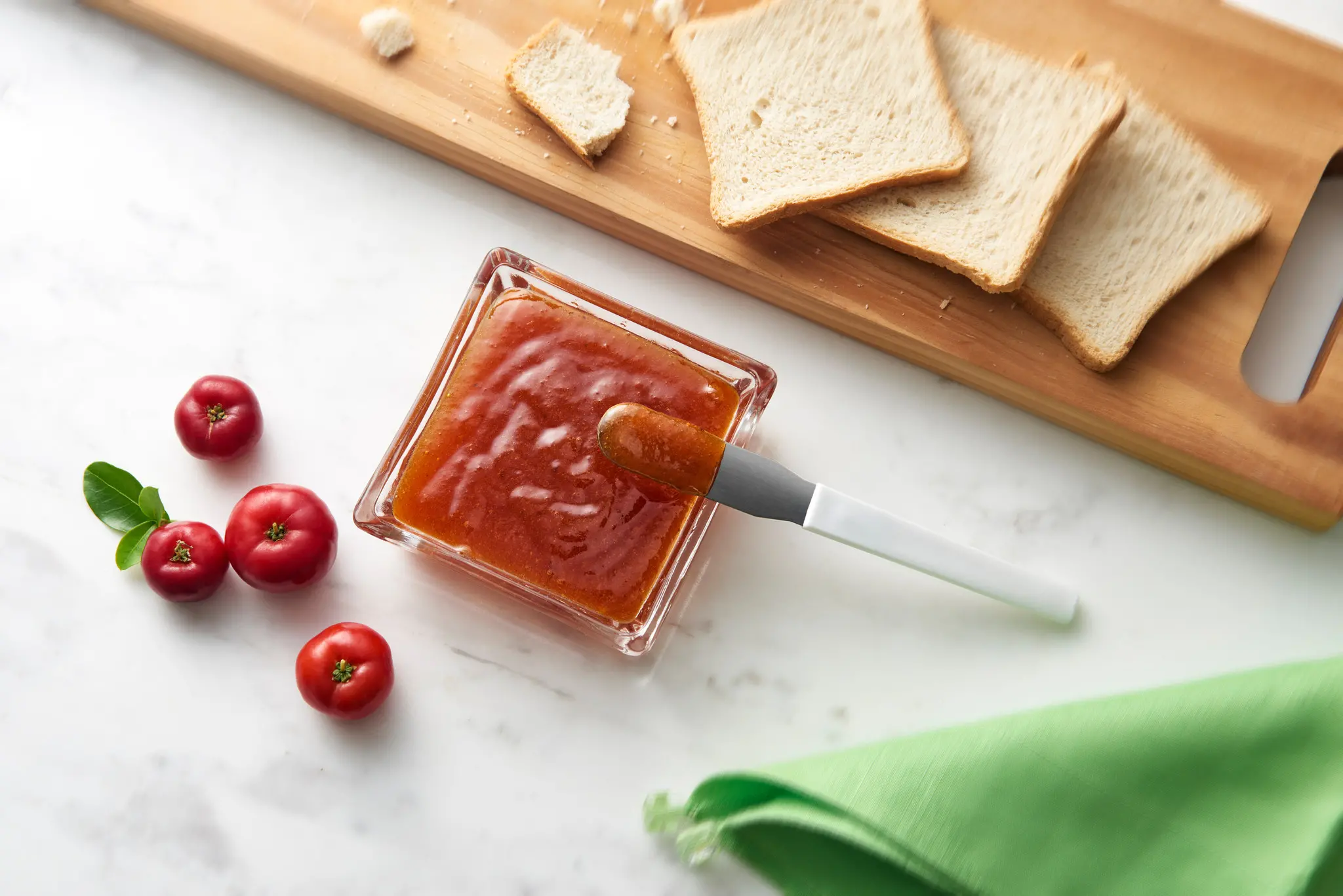 Geleia de acerola ao lado de algumas frutas e pães